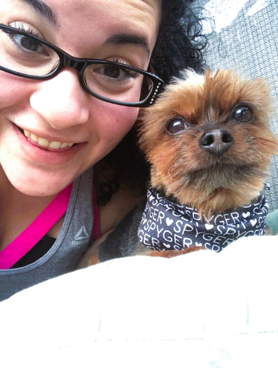 A woman wearing glasses smiling next to Spyger, her small dog